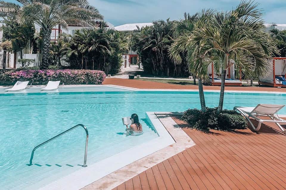 Turquoise resort pool with palm trees, lounge chairs, and mountain views