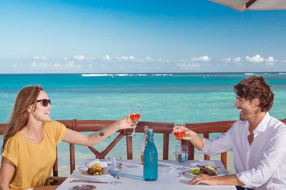 Couple toasting with glasses overlooking turquoise ocean from beachfront dining table