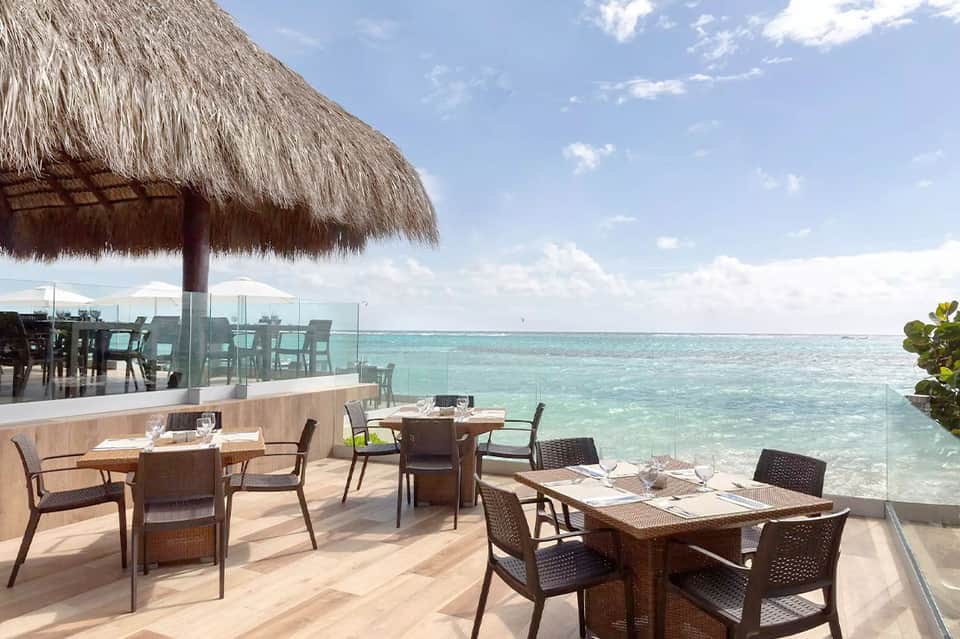 Beachfront restaurant terrace with thatched roof umbrella, tables, and turquoise ocean water view