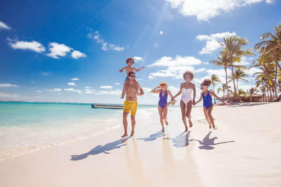 Family of four running on white sand beach with turquoise water and palm trees