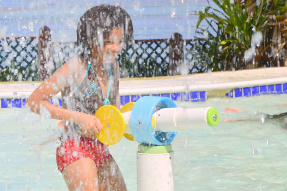 Child playing in shallow pool with colorful water toys and splash pad