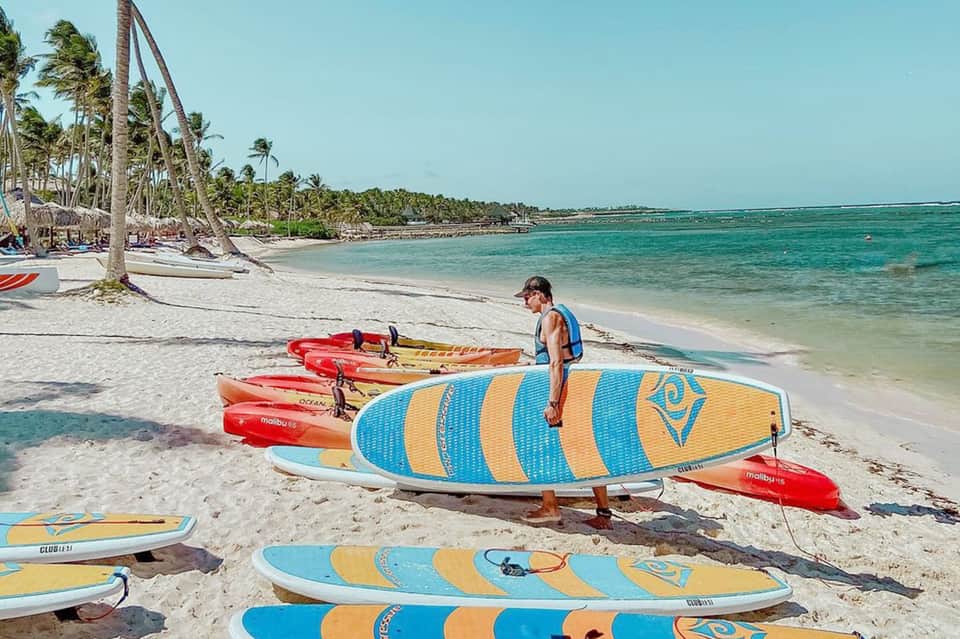 Colorful surfboards and paddleboards lined up on a tropical beach with palm trees and turquoise water