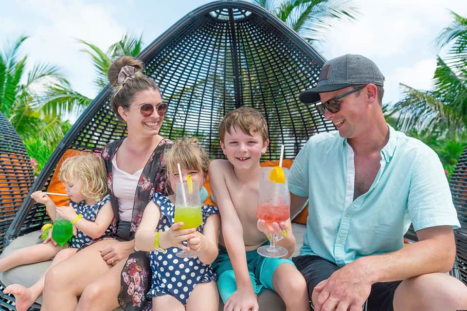 Family of four enjoying colorful drinks under a black dome umbrella by the pool