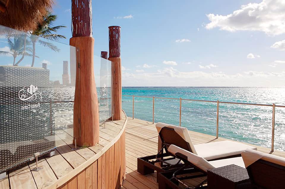 Wooden deck with lounge chair overlooking turquoise ocean waters with modern building visible