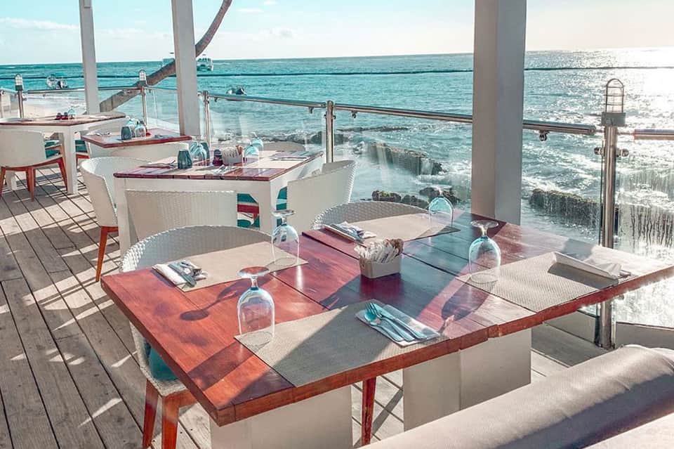 Oceanfront dining terrace with wooden tables, ocean views, and modern architectural elements