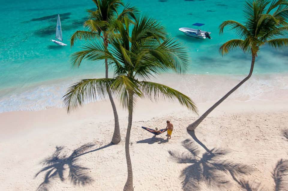 Aerial view of tropical beach with palm trees, sailboat, and turquoise ocean water