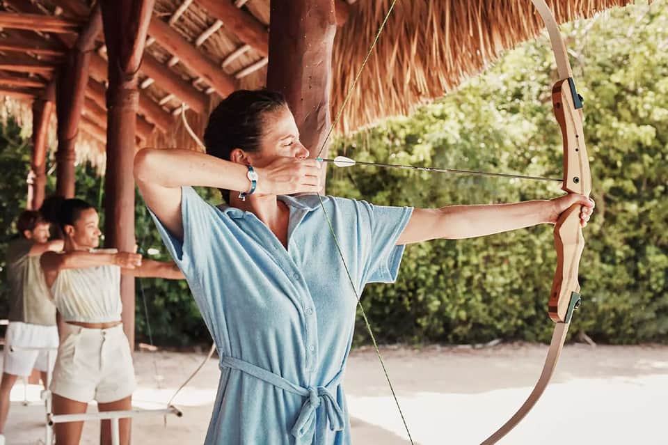 Woman practicing archery at beach resort under thatched roof structure