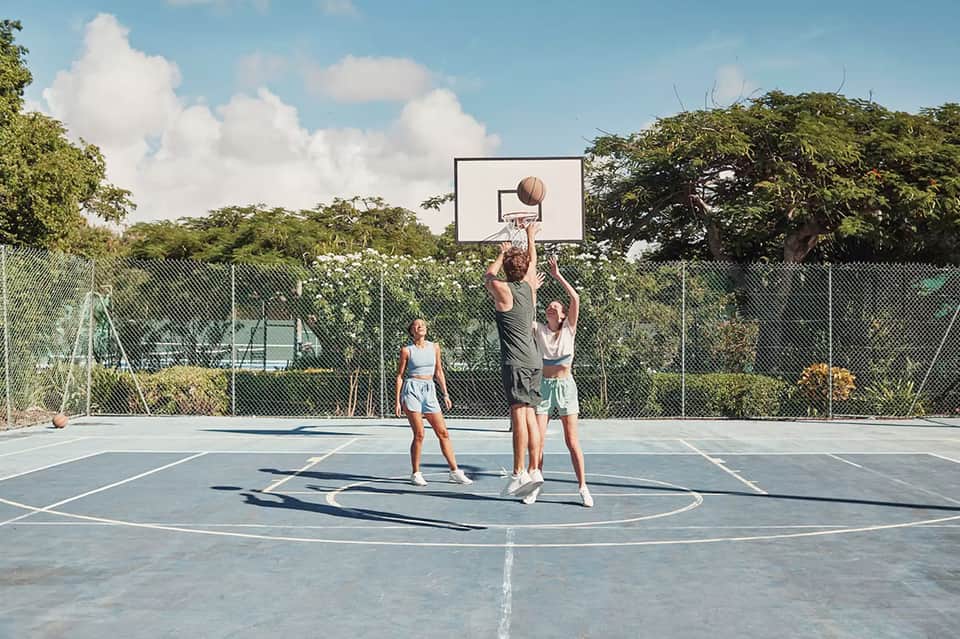 Young people playing basketball on an outdoor court with green landscape