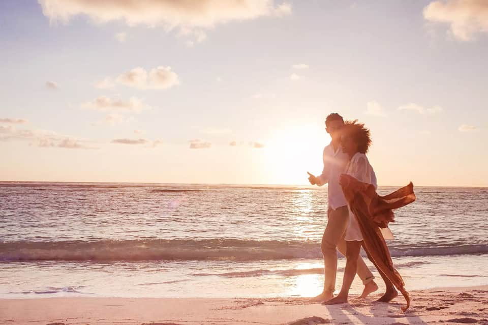 Couple running playfully on beach at sunset with ocean waves and golden sky