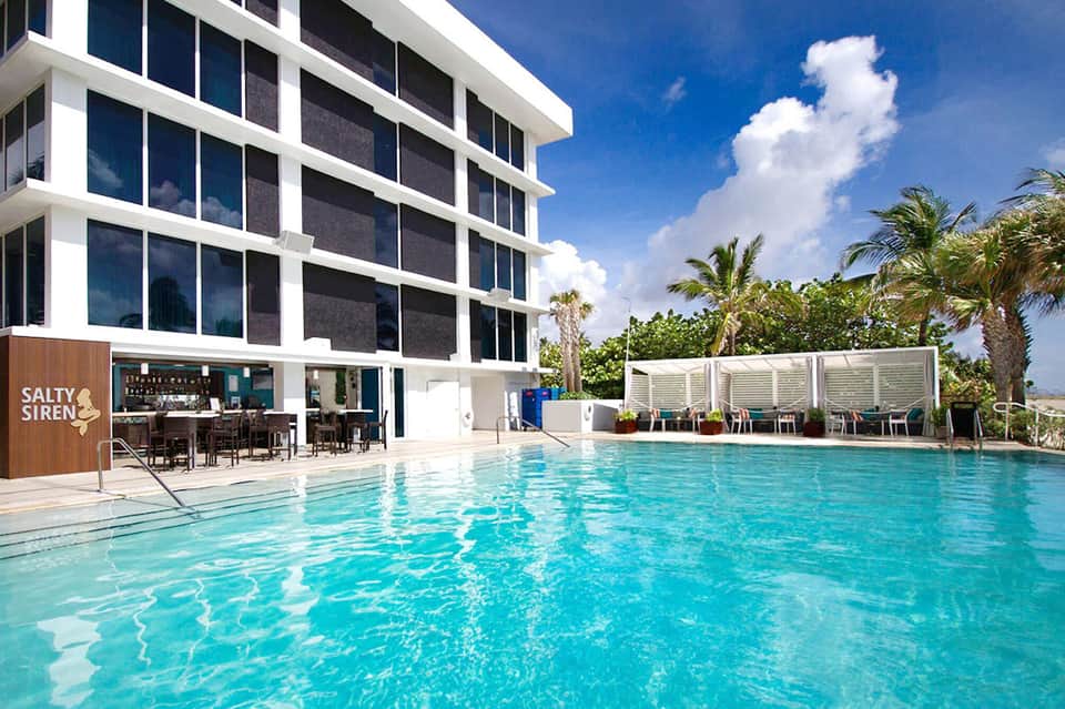 Contemporary hotel pool with turquoise water, modern building facade, and palm trees