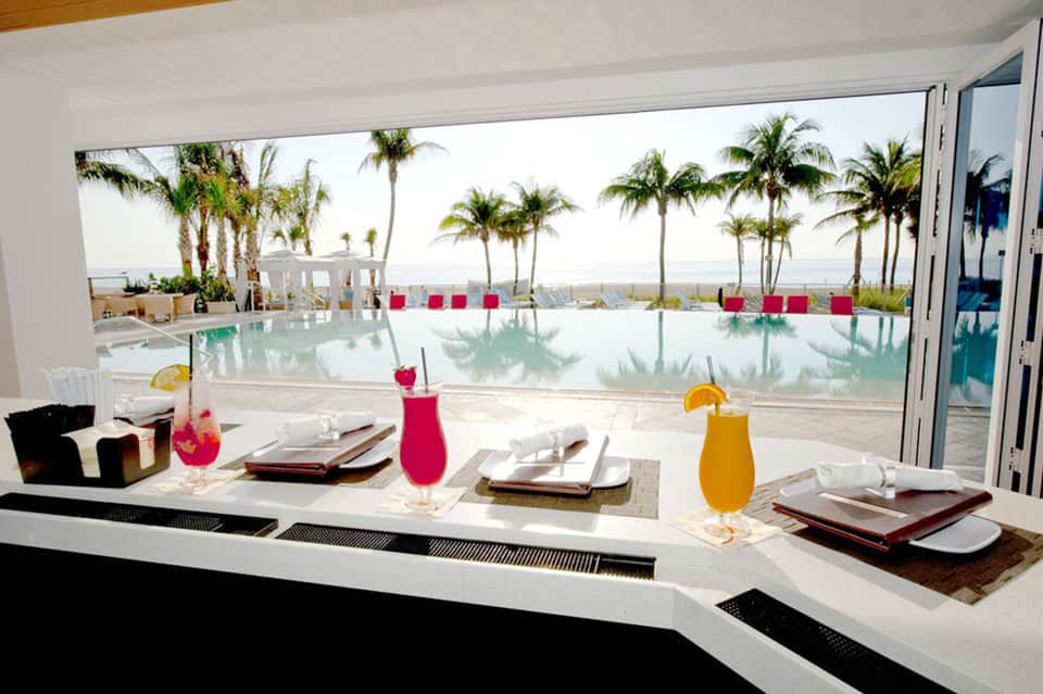 Upscale restaurant dining area with ocean and palm tree views through floor-to-ceiling windows
