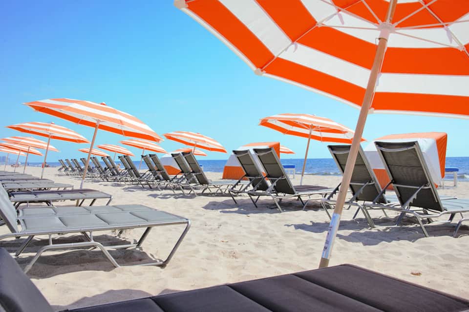 Beach scene with rows of orange and white striped umbrellas and gray lounge chairs on sand facing the ocean
