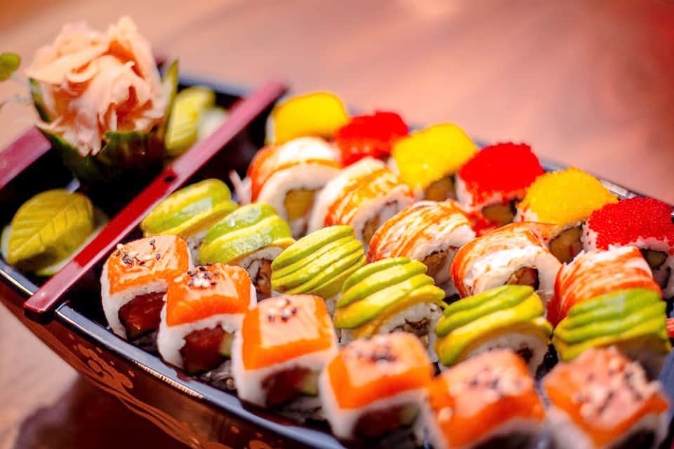 Colorful sushi rolls with salmon, vegetables, and garnish on a dark plate