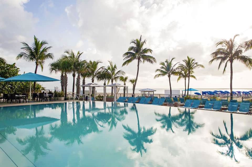 Resort infinity pool with palm trees and lounge chairs overlooking distant mountains at dusk