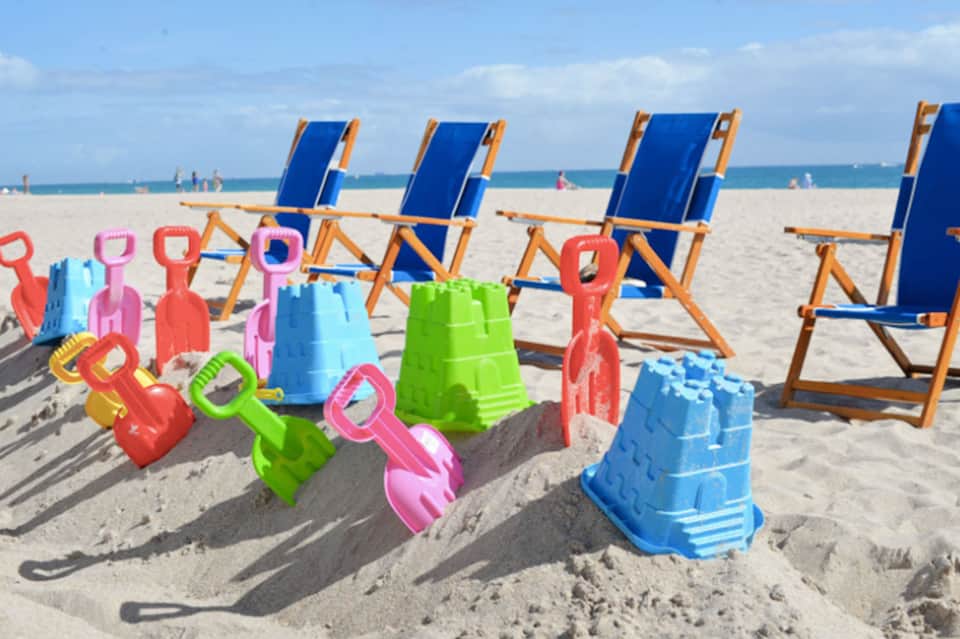 Colorful children's beach toys and sand buckets with blue beach chairs in background