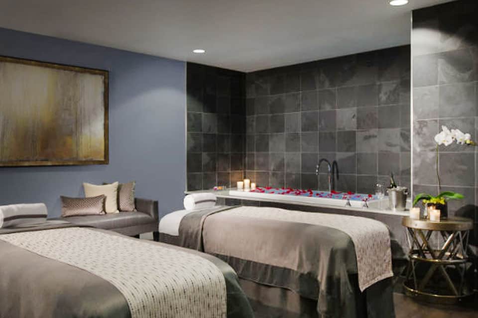 Luxury spa suite with two beds, soaking tub with candles, and relaxation seating area