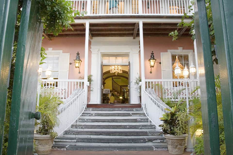 Colonial-style mansion entrance with pink walls, white columns, and symmetrical covered porches