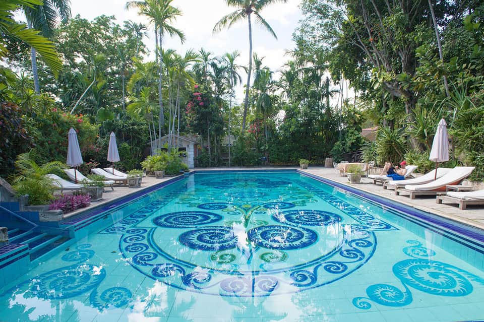 Resort pool with decorative blue tile patterns, palm trees, lounge chairs, and umbrellas
