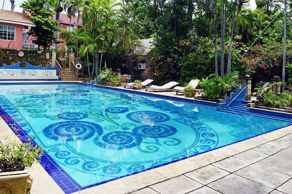 Ornate resort swimming pool with decorative blue tile patterns, surrounded by lounge chairs and tropical plants