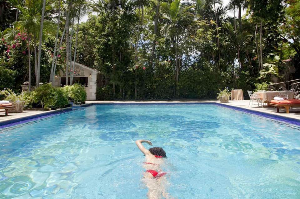 Child swimming in tropical resort pool surrounded by lush green vegetation and palm trees