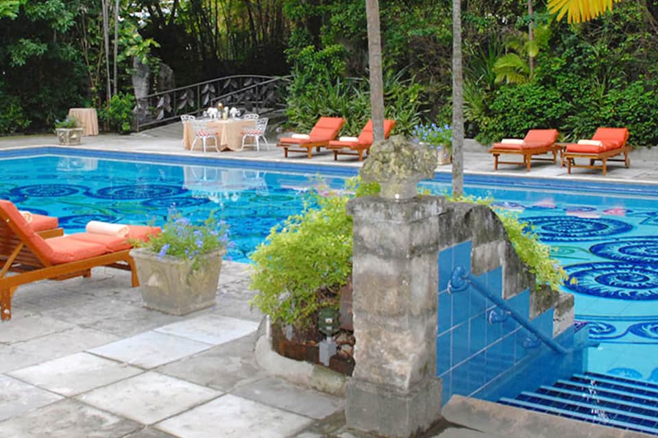 Resort pool with blue decorative tile pattern surrounded by lounge chairs and lush tropical vegetation
