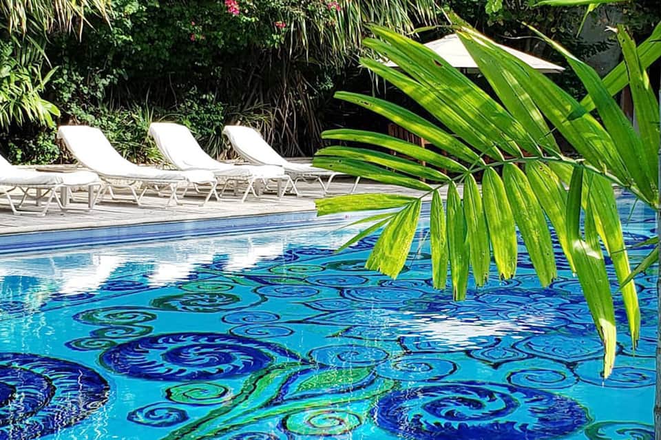 Decorative pool tile design with tropical palm fronds and lounge chairs nearby