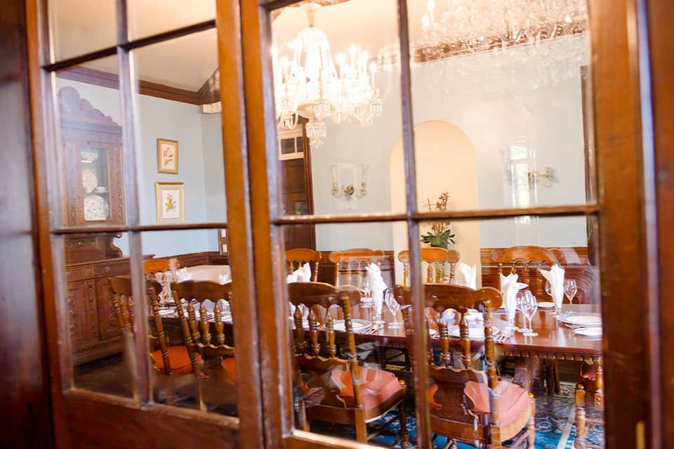 Elegant dining room viewed through glass doors with wooden furniture, chandelier, and formal place settings