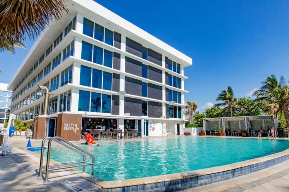 Resort pool area with turquoise water, modern white building, and palm trees