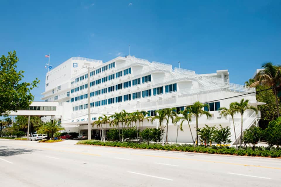 Modern white multi-story hotel building with palm trees and clear sky in tropical location