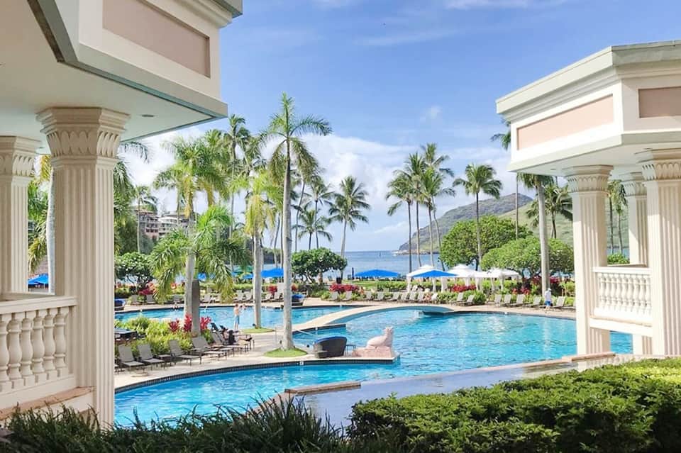 Luxury resort pool with neoclassical columns, ocean view, and palm trees framing the scene