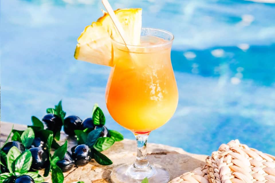 Tropical cocktail with pineapple garnish served poolside with blue water background