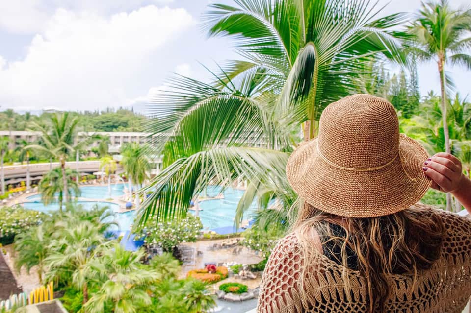 Woman in straw hat overlooking lush resort grounds with pools and palm trees