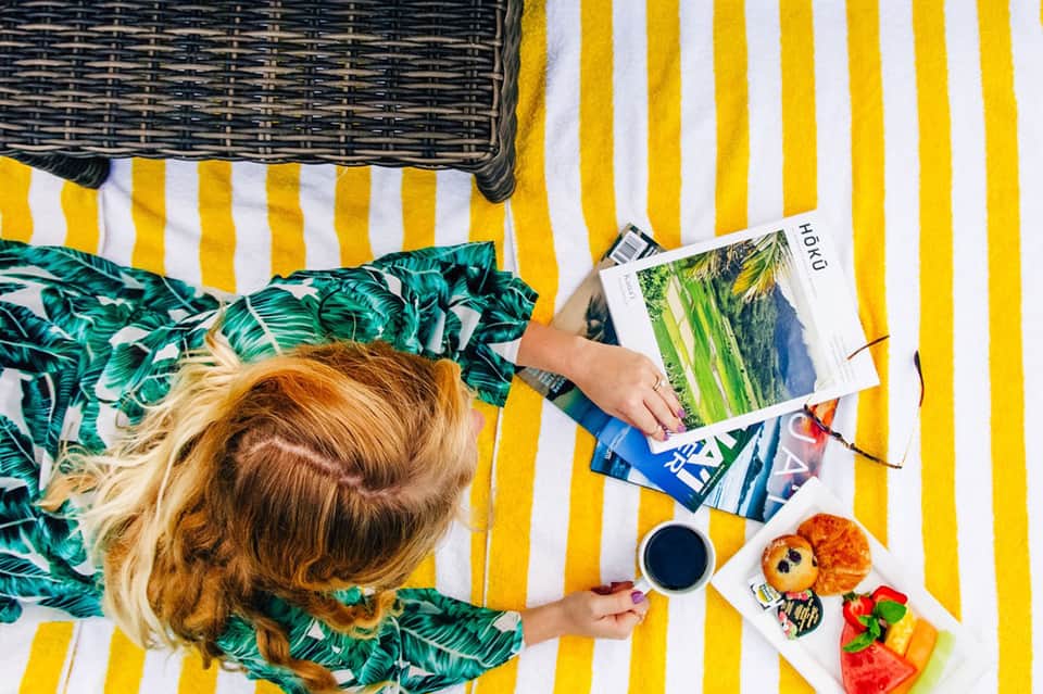Overhead view of woman reading on yellow striped lounger with tropical snacks and beverage