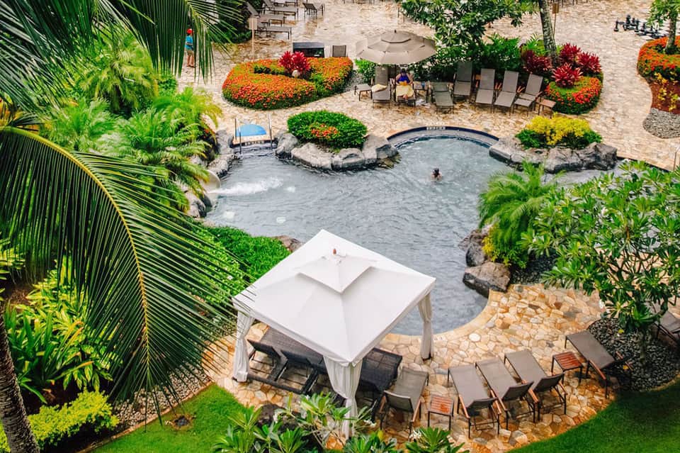 Aerial view of tropical resort with natural hot spring pool, white cabana, lounge chairs, and lush gardens