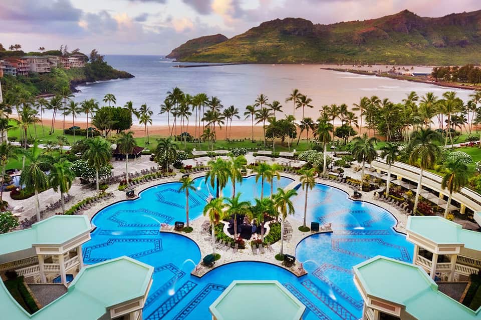 Aerial view of resort with blue pools, palm trees, and sandy beach with ocean beyond