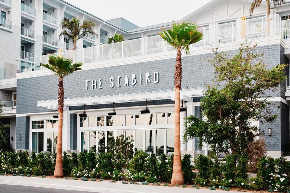 The Seabird restaurant entrance with white brick facade, palm trees, and manicured landscaping