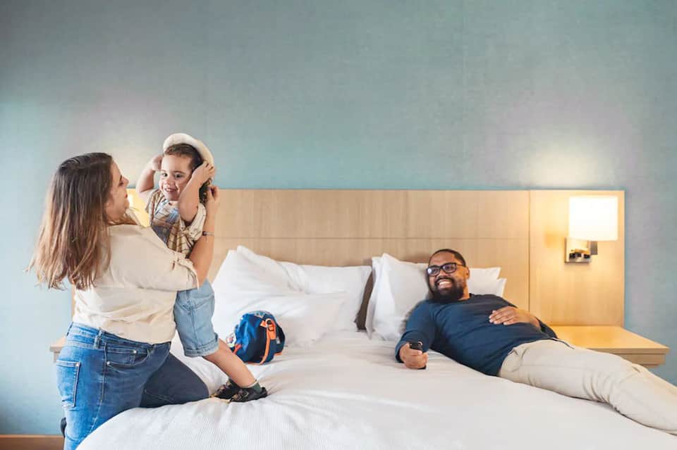 Family in modern hotel room with parents and child on bed with contemporary furnishings