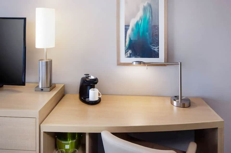 Modern hotel room desk with lamp, coffee maker, and ocean wave artwork on wall