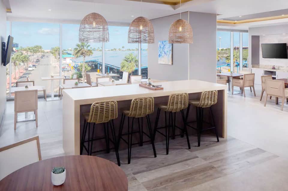 Contemporary hotel bar with woven pendant lights, ocean view windows, and woven rattan barstools