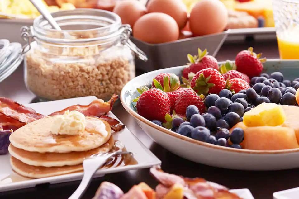 Breakfast spread with pancakes, bacon, fresh berries, eggs, cereal, and orange juice
