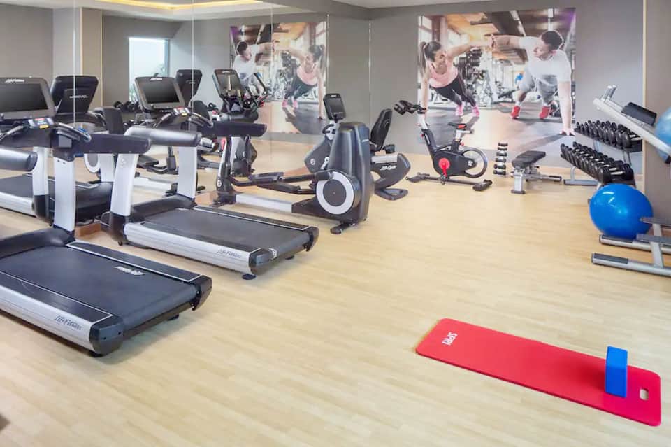Modern fitness center with treadmills, stationary bikes, dumbbells, and mirrored walls with exercise equipment