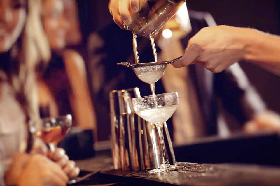 Bartender pouring cocktails into martini glasses at an evening bar service