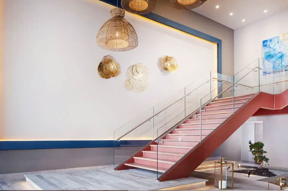 Modern hotel staircase with coral steps, woven pendant lights, and artistic wall decor