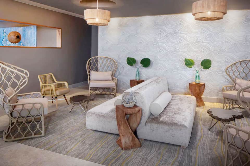 Modern spa lounge with white furniture, woven chairs, pendant lighting, and botanical wall décor
