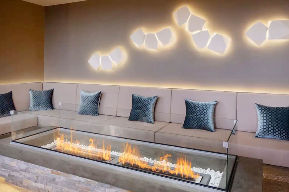 Modern lounge with curved cream sofa, fireplace, geometric wall lights, and blue pillows