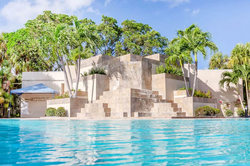 Modern resort pool with geometric concrete wall and palm trees under clear blue sky