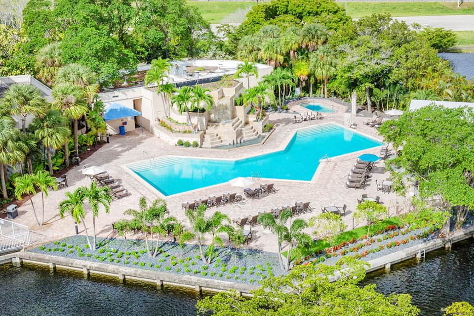 Aerial view of tropical resort with large turquoise pool, palm trees, waterfront gardens, and lounge chairs