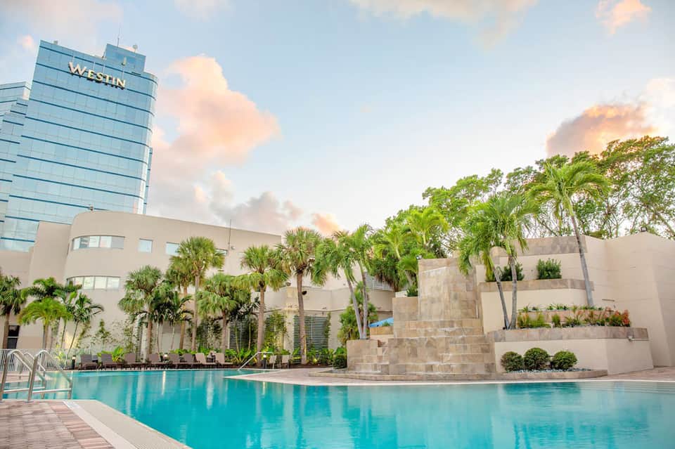Modern Westin hotel with turquoise pool, palm trees, stone water feature, and glass tower
