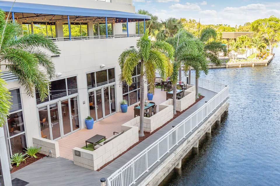 Modern waterfront building with terrace, palm trees, and river views