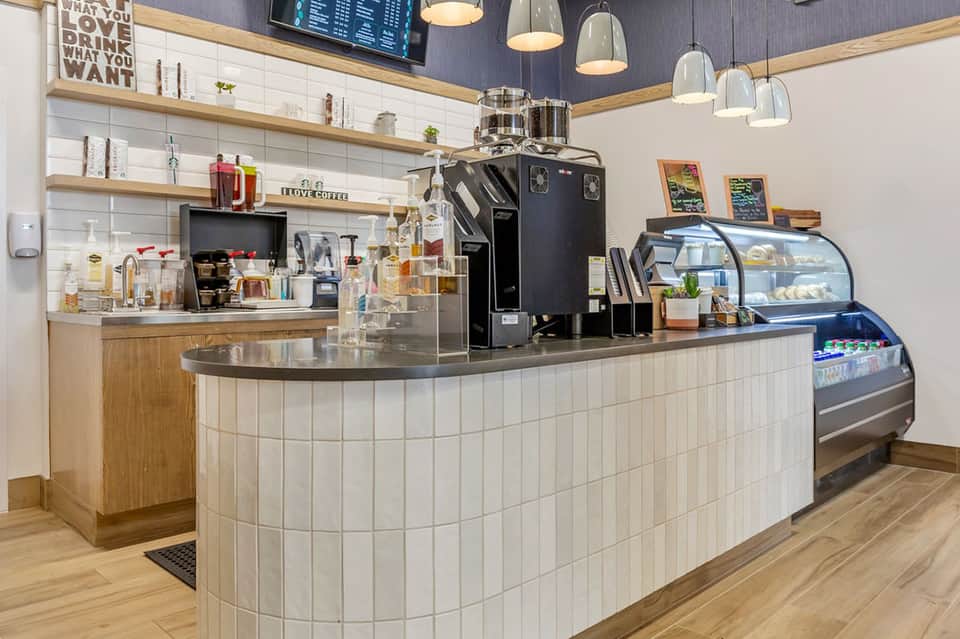 Contemporary coffee shop counter with espresso machine, pastry case, and wooden shelving